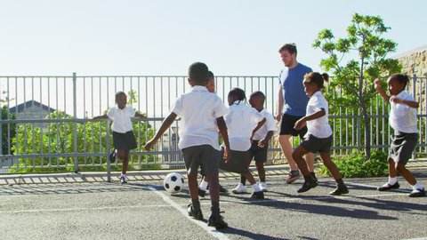 Teacher plays football with young kids in school playground Stock Video
