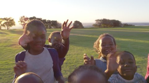 Elementary school kids waving to camera outdoors, close up