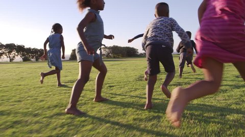Elementary school kids chasing football in a field