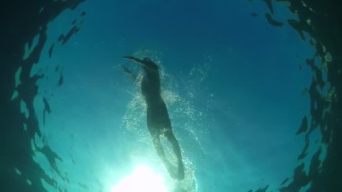 SLOW MOTION CLOSE UP UNDERWATER LOW ANGLE VIEW: Fit muscular guy swimming freestyle stroke in amazing open ocean on stunning sunny summer day. Sunlight penetrating crystal clear water and sea surface