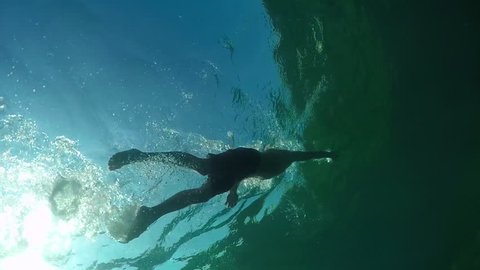 SLOW MOTION CLOSE UP UNDERWATER LOW ANGLE VIEW: Athletic muscular guy swimming freestyle stroke in amazing green crystal clear ocean with rocky coral sea floor. Guy enjoying relaxing sunny summer day