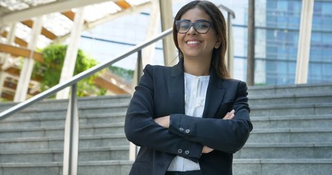 Portrait of young beautiful business woman (student) in suit, glasses, smiling, happy, walking down stairs, steps, on building background. Concept: new business, communication, Arab, banker, manager.