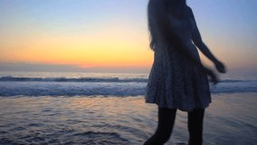 Silhouette of young attractive Indian American woman wearing Retro style sundress enjoying sunset dancing on the beach