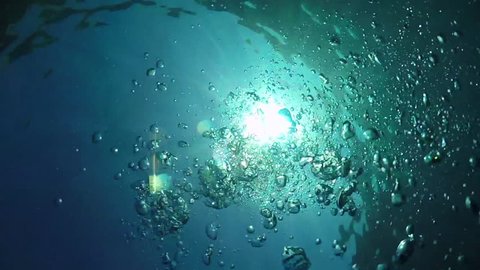 SLOW MOTION UNDERWATER CLOSE UP: Numerous small air bubbles rising up to surface in turquoise tropical sea. Warm sunshine penetrating crystal clear ocean water on sunny summer day. Person drowning