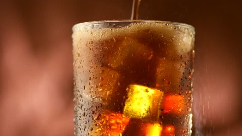 Pouring Cola with ice cubes Cola drink with Ice and bubbles and water drops on glass. Soda closeup. Brown background. Rotation Fizzy drink. 4K UHD video footage. Ultra high definition 3840X2160 