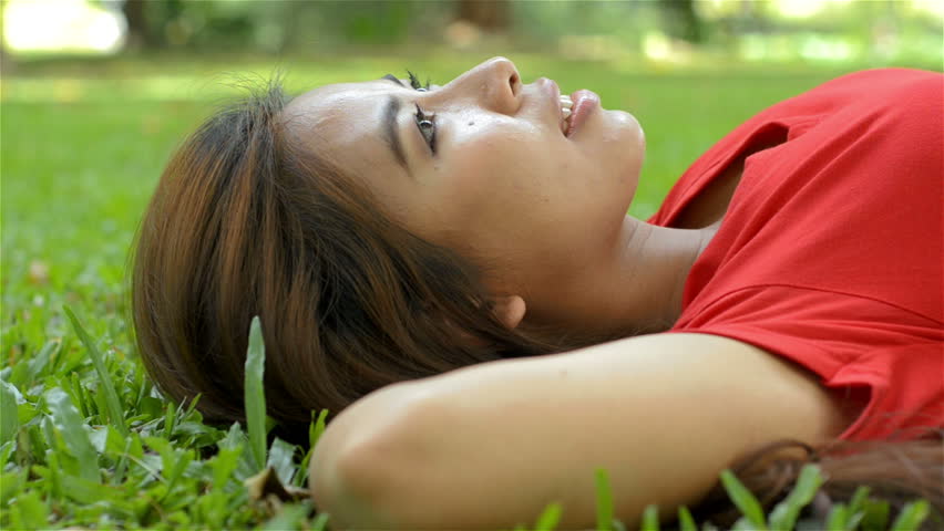 Young Asian woman relaxing lying on the grass in a park, with her arms behind
