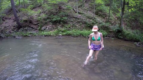Bikini clad mature woman hiking through natural mountain stream or creek in forest, captured with