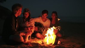 Picnic of young people with bonfire on the beach in the evening. Cheerful friends singing songs and playing guitar. Slowmotion shot - Powered by Shutterstock - Get 15% off with code: PIKWIZARD15