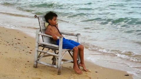 Young boy relaxing in the armchair on the tropical beach