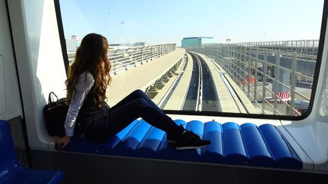 Young adult woman sit against front window at inter-terminal train, look outside. Leonardo da Vinci airport connection between buildings, international arrival passage. Sunny day outdoors