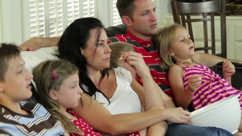 Mom and dad and four children enjoy watching TV together. close shot.