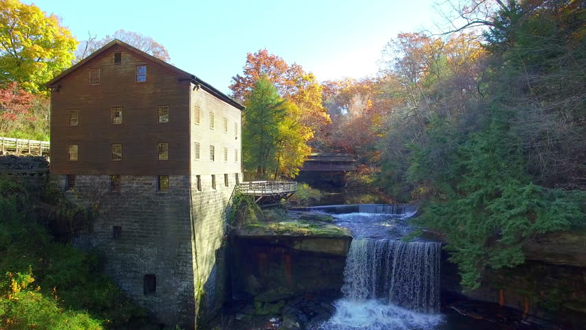 Colorful fall day flyover over of river with water wheel and covered bridge.