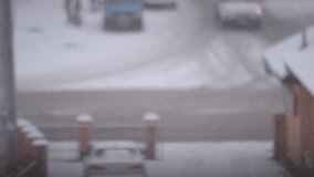 Snow falls on blurry city road landscape background with cars driving by and people passing by