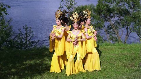 group of five asian women actresses in traditional chinese yellow costumes dancing beautiful dance at the river bank