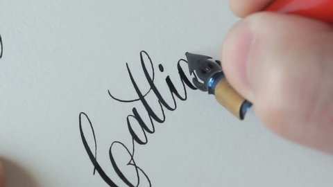 Calligrapher writing a word Calligraphy with point nib pen and black ink on white paper.