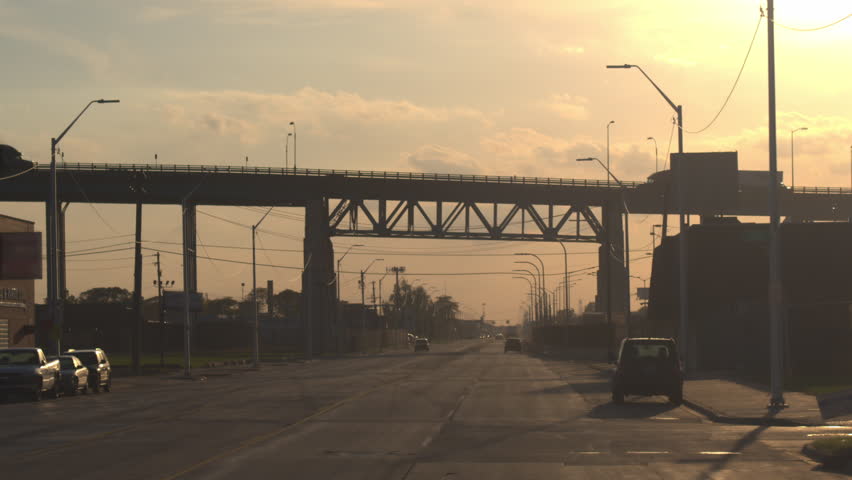 CLOSE UP, FPV: Semi trucks driving over the overpass, transporting goods across the busy multiple lane highway full of cars at golden sunrise in industrial city Detroit, America.