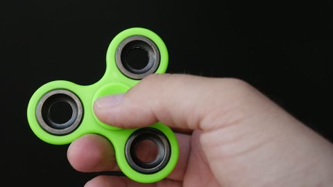 Close up footage of a persons hand playing with the fidget spinner, isolated on a black background...