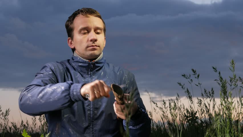 Man prepares wood-wool with hunting knife for starting fire at sunset on the field. Wood shaving. Survival concept