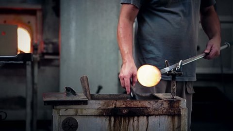 Man working glass with fire and blowing through the pipe