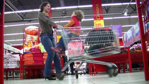 mother rotates child in shopping cart in shop 