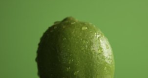 lime turning on it's axis on green background covered by water drops. texture footage