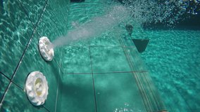 Underwater perspective of a nozzle spewing water and bubbles through an outlet in the blue. tiled wall of a swimming pool. Video 4k UltraHD