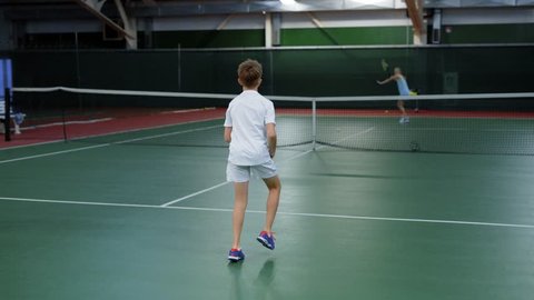 Sports training on tennis for teenagers, children throw the ball through the net with the help of rackets, active movements on the court in the gym