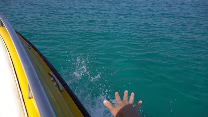 Male hand above turquoise sea water. POV shot from motor boat