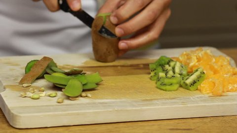 Chefs hands slice fruits on wooden cutting board. Summer vegan fruits salad