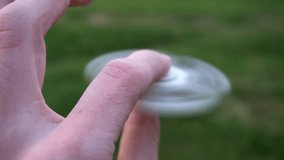 white hand spinner, or fidgeting spinner, rotating on child's hand.grass background. Slow motion