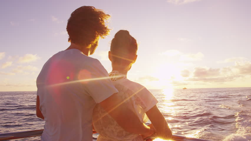 Cruise ship vacation couple enjoying sunset view sailing on small cruise boat at sea. Romantic couple on honeymoon travel at sea looking at sunset.  SLOW MOTION.