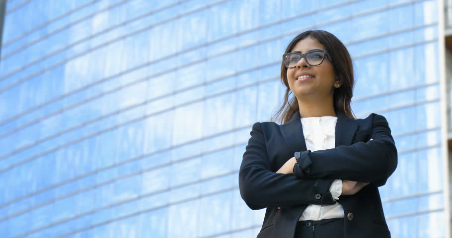 Portrait of young beautiful business woman (student) in suit, glasses, smiling, successful looking at sides, with skyscraper background. Concept: new business, communication, Arab, banker, manager. | Shutterstock HD Video #28148323