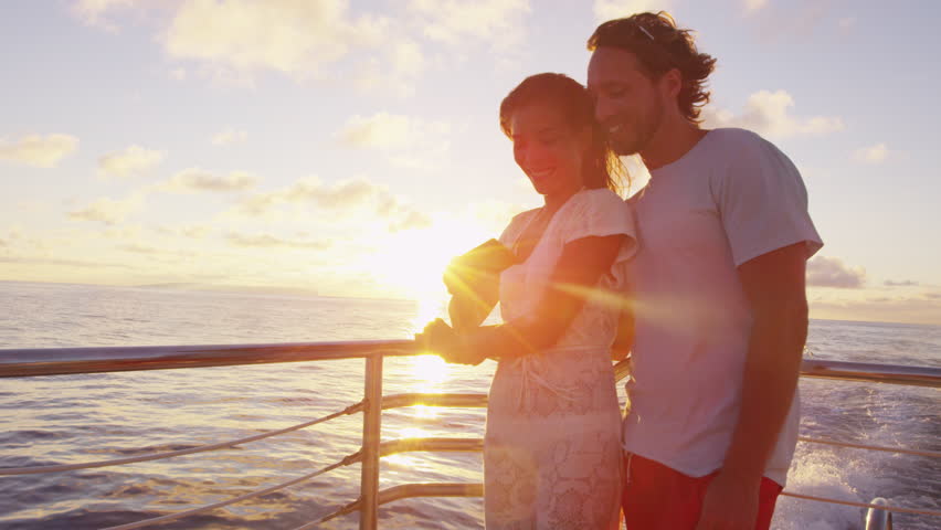 Couple using smart phone screen on sunset cruise ship sailing in ocean on vacation. Woman and man looking at smartphone app having fun on travel.
