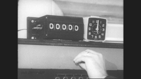 1960s: UNITED STATES: man flicks switch. Numbers on screen. Clock by counter.