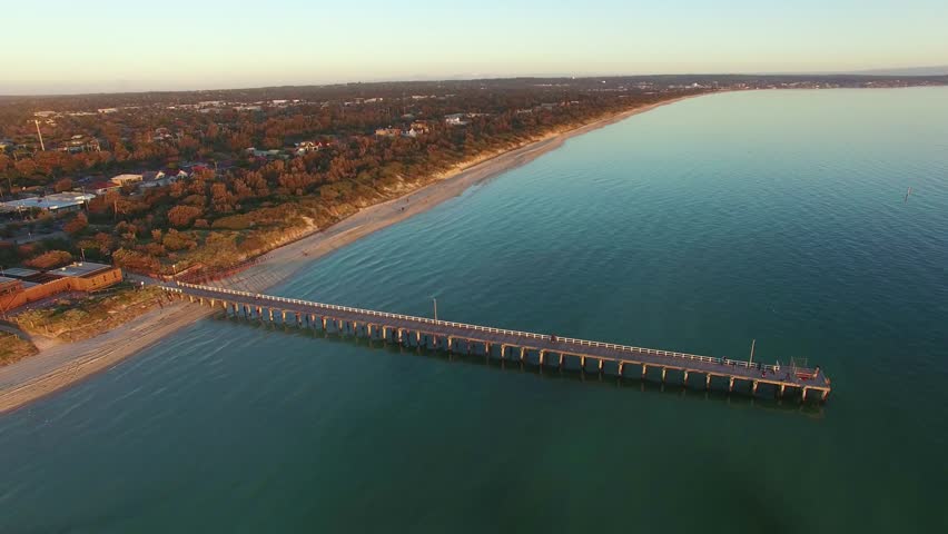 Aerial flight around long ocean pier at sunset. Melbourne, Victoria, Australia