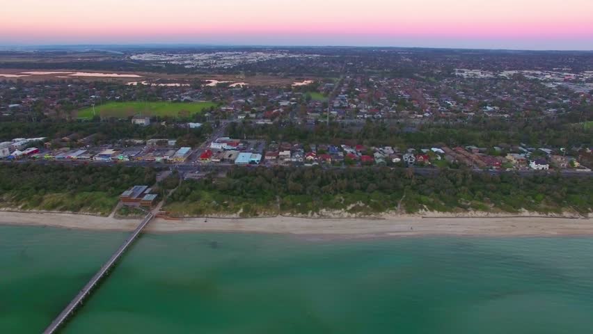 Horizontal flight along Melbourne Coastline passing long wooden pier at beautiful sunset.
