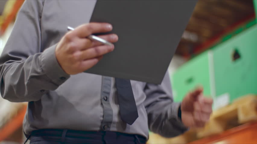 Low angle of businessman in shirt and tie walking in slow motion along shelves in warehouse and writing on clipboard | Shutterstock HD Video #28153747