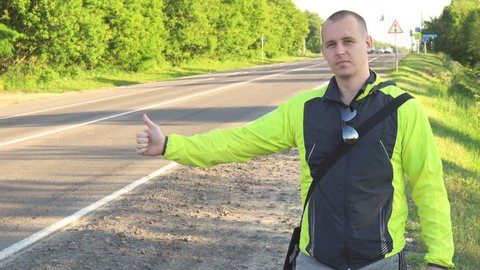 Hitchhiking traveling young adult man displaying Everywhere written sign board pointing thumb up on interstate highway.