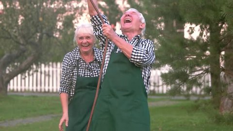Senior couple having fun outdoors. Cheerful people with water hose. Old and crazy.