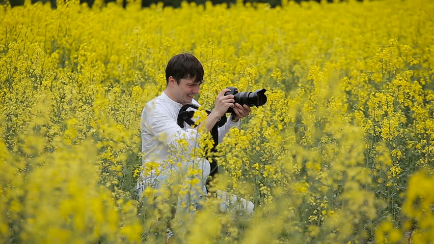 Photographer with a camera taking pictures in a blooming yellow field