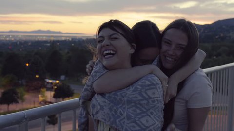 Happy Girls Have Group Hug And Laugh Really Hard At A Viewpoint, City And Mountains In Background 