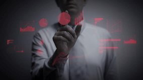 A businessman working on a red holographic interface, touching a hologram showing a visual screen with computer and business icons. Financial charts and graphs appear. The touchscreen illuminates. 4K - Powered by Shutterstock - Get 15% off with code: PIKWIZARD15