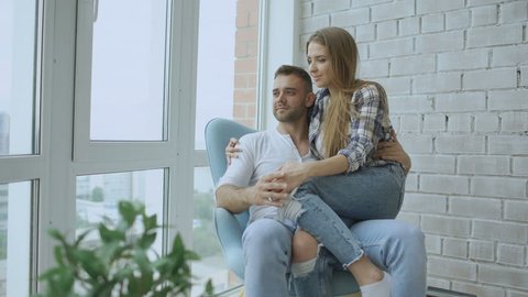 Beautiful young couple relax sitting on chair and enjoying view from balcony of new loft apartment