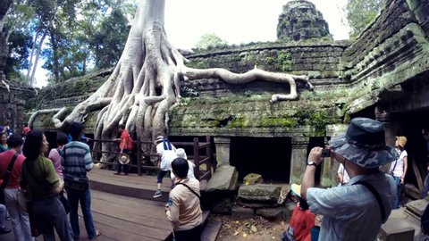 SIEM REAP, CAMBODIA - OCTOBER 30, 2014: Streams of tourists take turns posing in time-lapse in front of the Ta Prohm temple in the Angkor complex, which suffers from overcrowding.