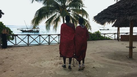 Two Masai people dances their national African dance on the Indian Ocean beach at sunset and bids farewell to the sun. Tanzania. Zanzibar. Slow motion. 4K.