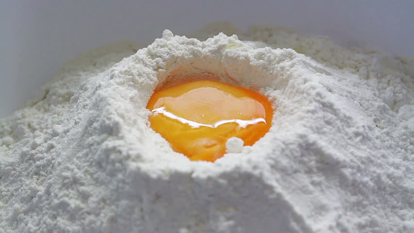 Fresh yellow egg being broken and  dropped down into white baking flour