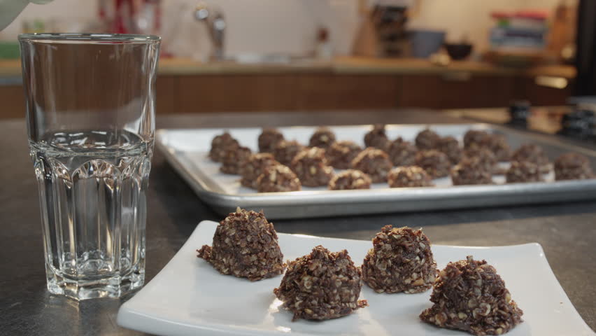 Close up of a plate of cookies while a glass of milk is being poured. Background shows a tray of cookies cooling.