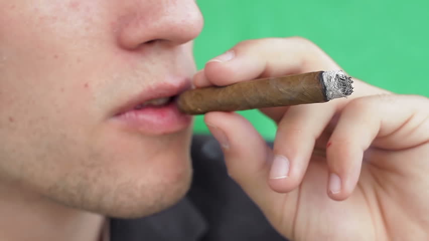 Young caucasian man starting off and smoking cigar on green background