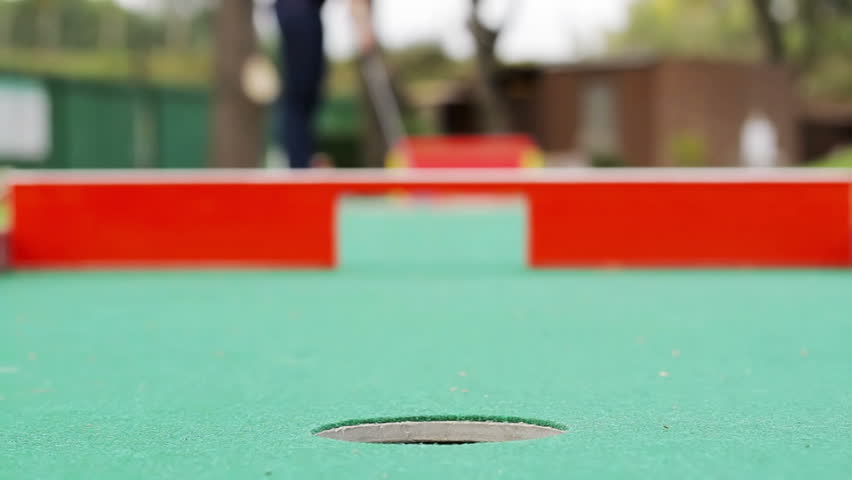 Young woman playing mini-golf during cloudy day, selective focus, failed attempt
