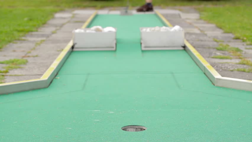 Young woman playing mini-golf during cloudy day, selective focus, failed attempt